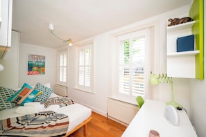 A bedroom with a bed, a desk, a lamp, a radiator, and a window with blinds. - Colourful Highbury Flat near Emirates Stadium - Pass the Keys (London)
