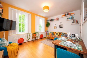 Una sala de estar con un sofá, una mesa de comedor, un televisor y una estantería.