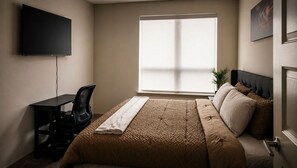 Ein Schlafzimmer mit einem Bett, einem Schreibtisch, einem Stuhl, einem Fenster und einem Fernseher.