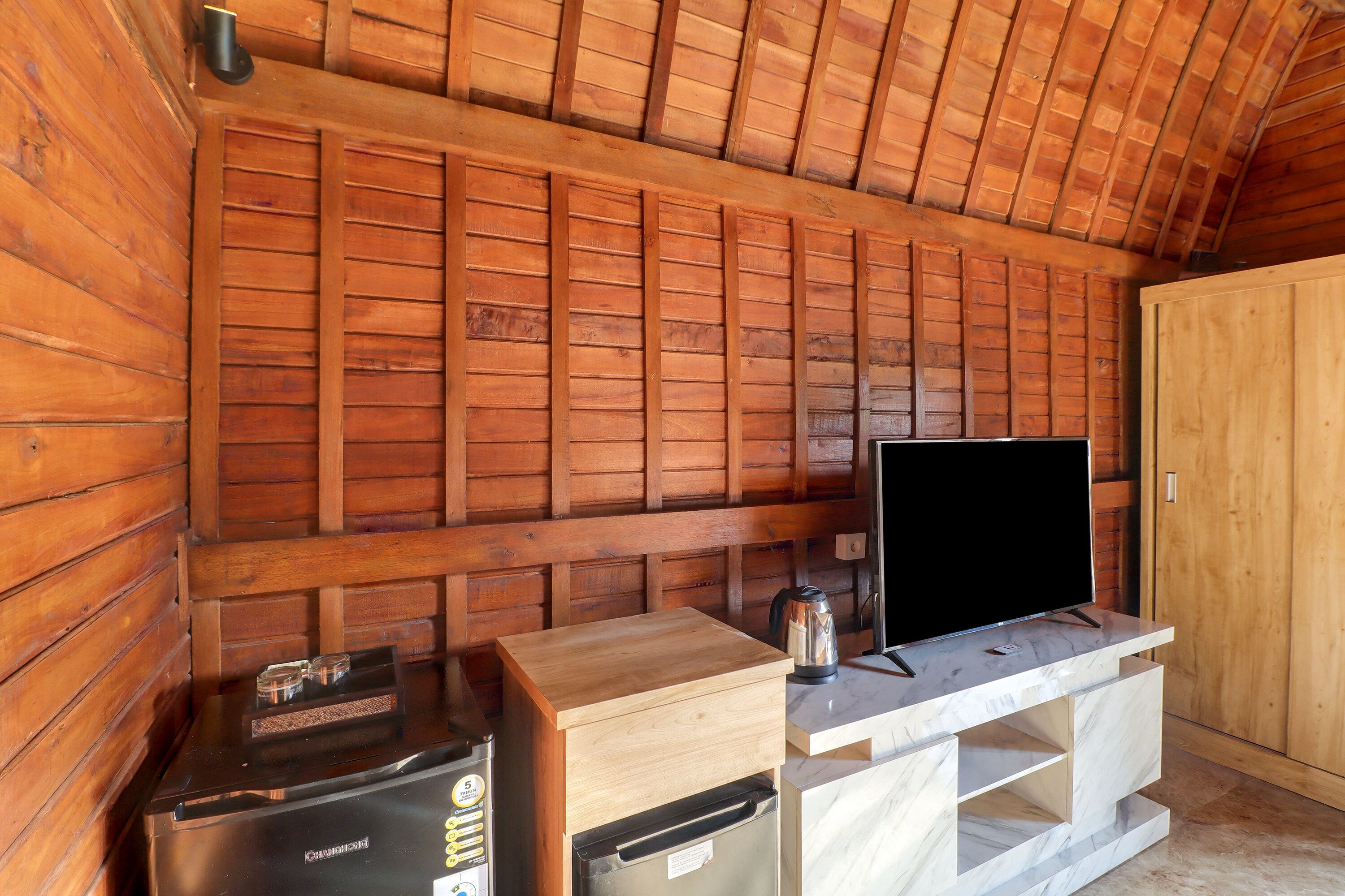A wooden cabin interior with a wooden wall, a television on a marble stand, a coffee maker, and a refrigerator.