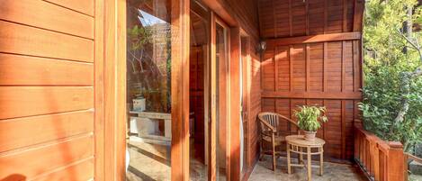 Een houten balkon met een tafel, stoelen, een hanglamp en een bloempot.