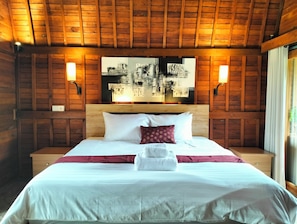 A wooden-paneled room with a bed, two wall-mounted lamps, and a cityscape artwork on the wall.