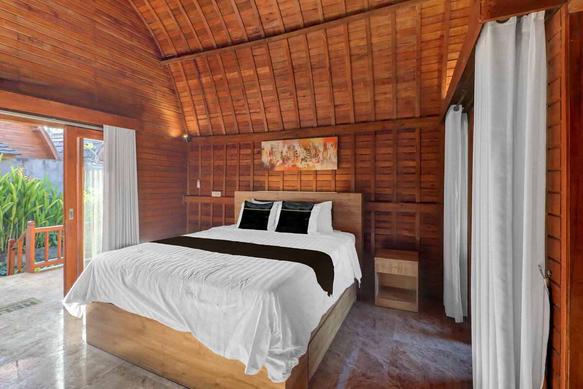 A wooden-paneled room with a bed, a nightstand, and a painting on the wall.