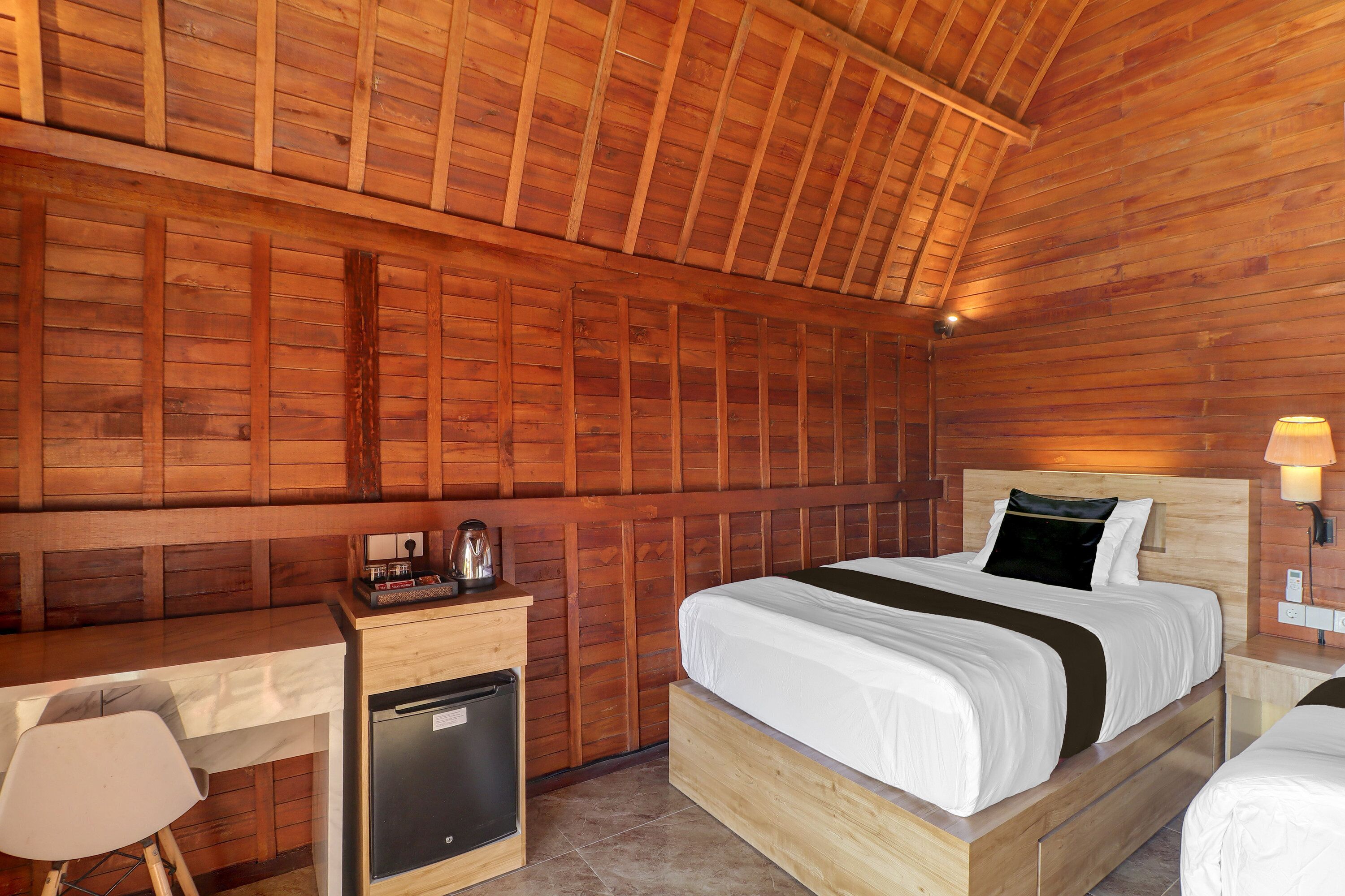 A wooden cabin room with a bed, a desk, and a refrigerator.