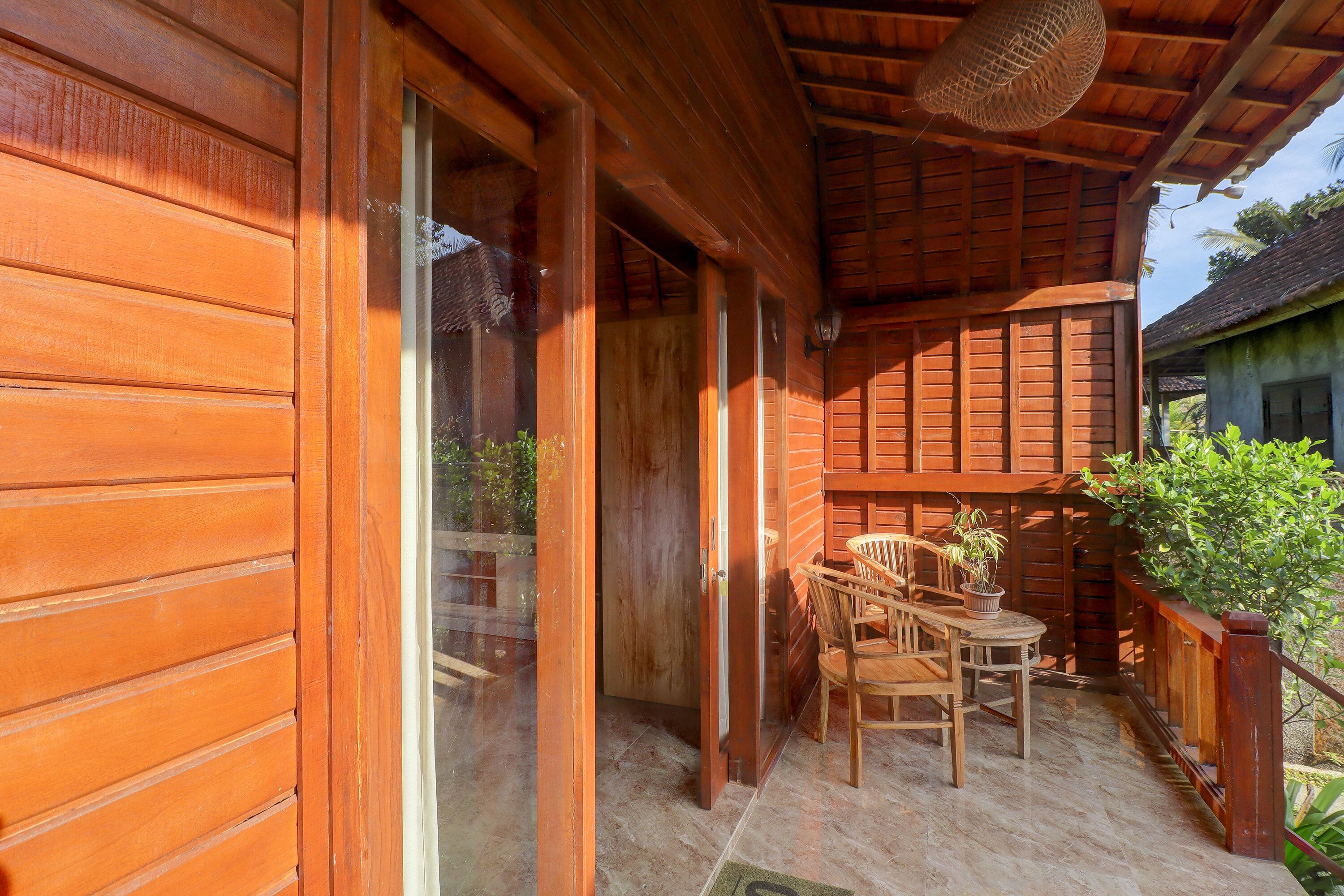 A wooden exterior with a sliding glass door, a covered patio with a table and chairs, and a potted plant.