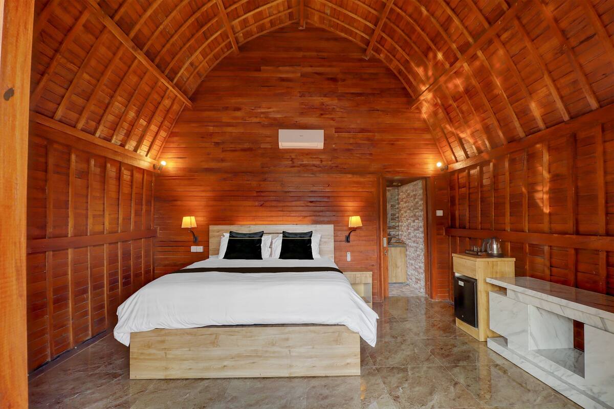 A wooden room with a bed, bedside lamps, a small wooden cabinet, and a marble countertop.