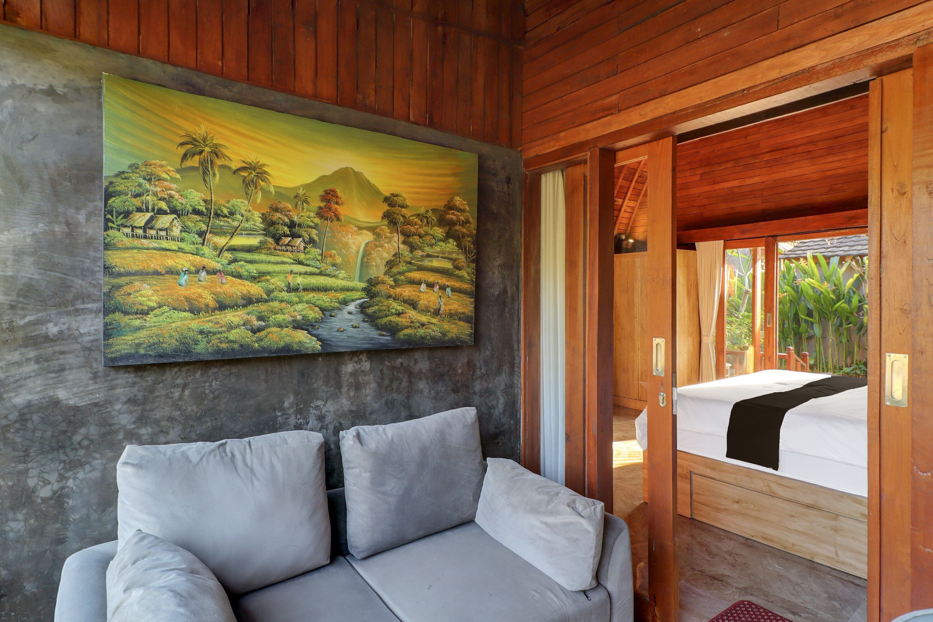 A room with a painting of a landscape, a sofa, and a bed.