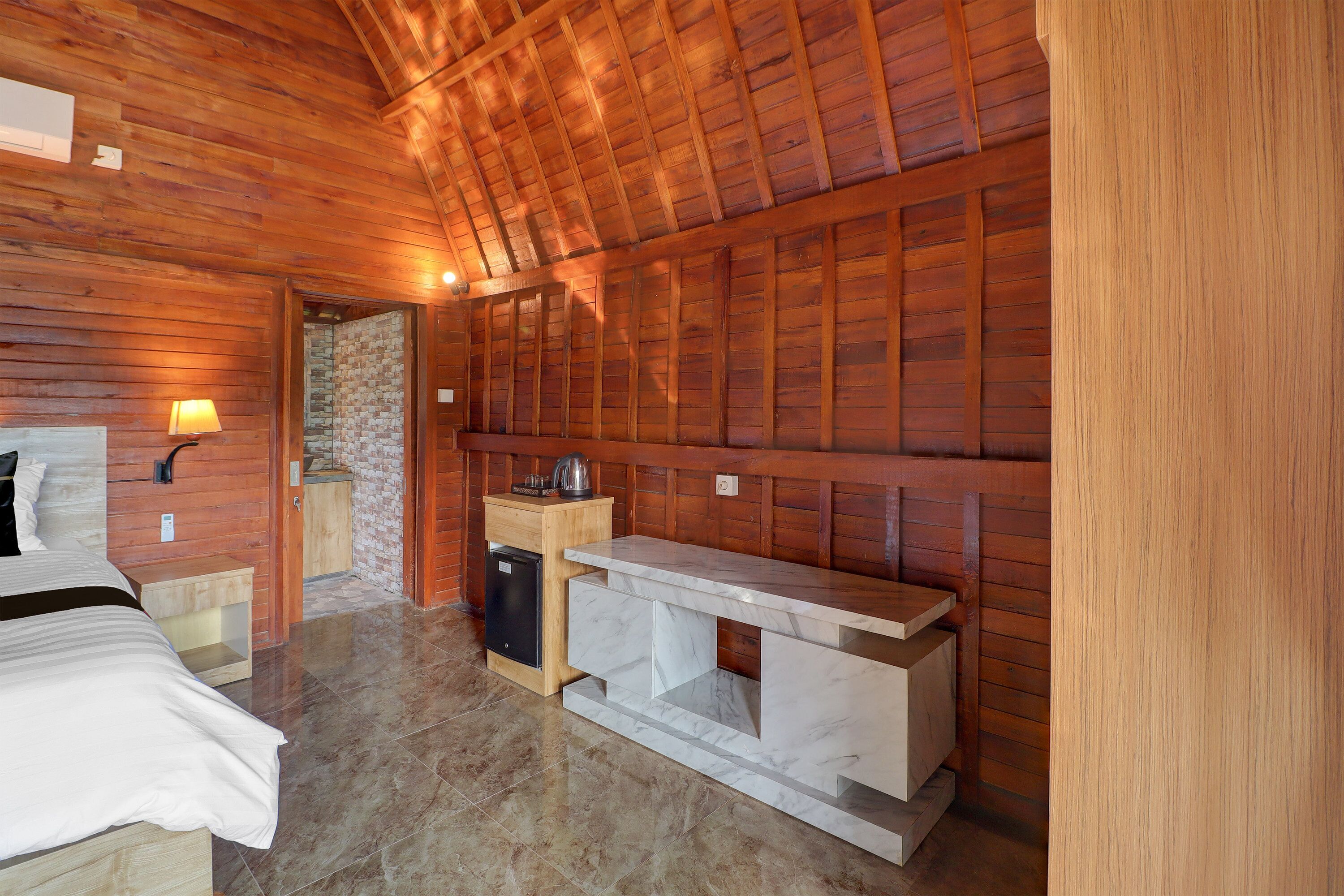 Una habitación con paneles de madera, una cama, un pequeño mueble de madera, una encimera de mármol y una chimenea de piedra.