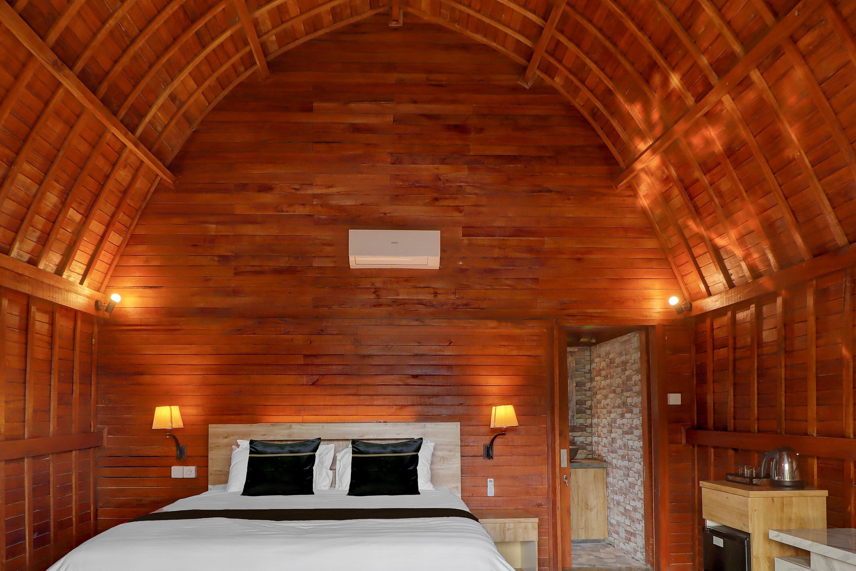 Una habitación con paneles de madera, una cama, dos lámparas de pared y una pequeña kitchenette.