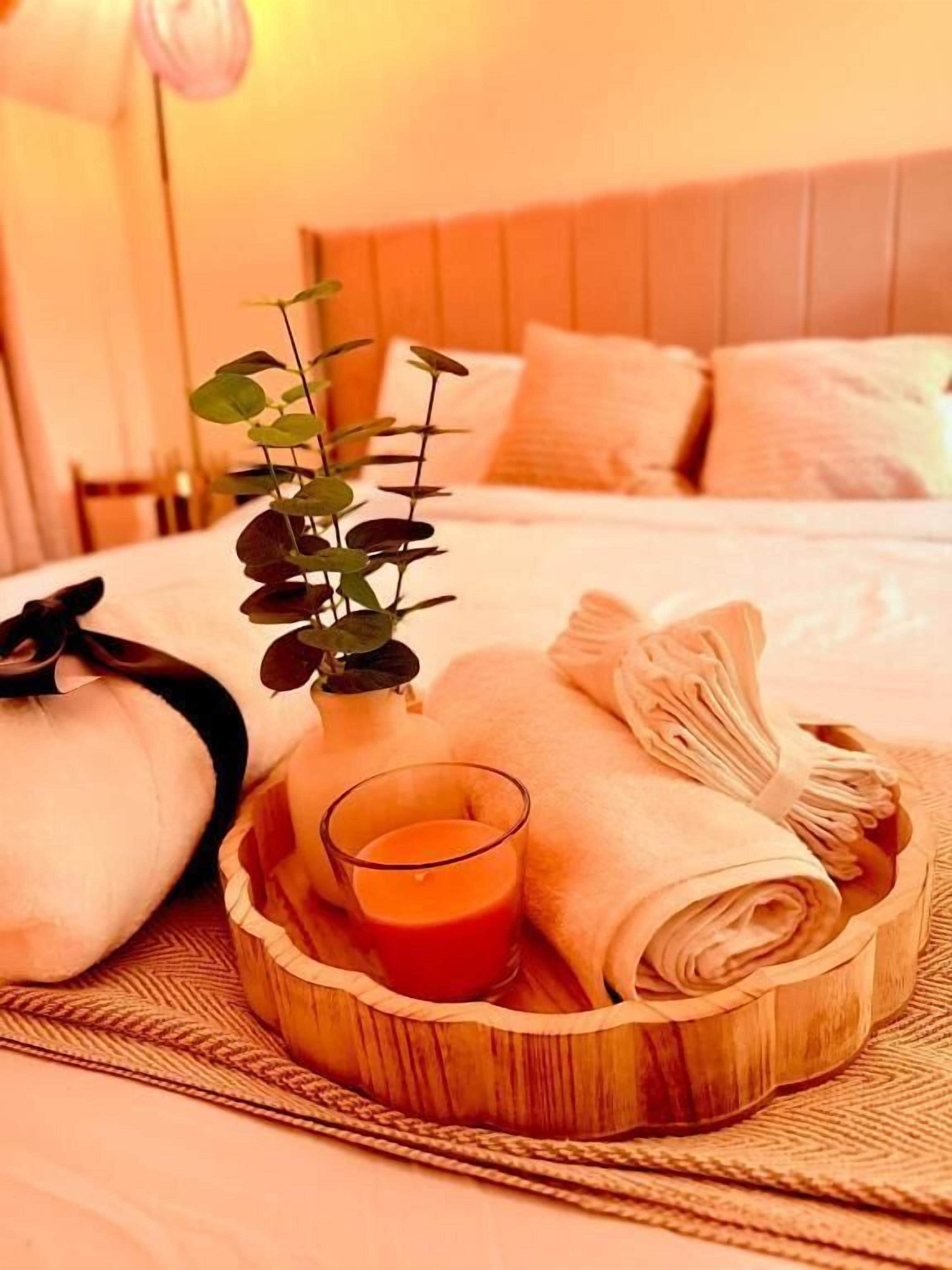 A neatly arranged bed with a wooden headboard, a small potted plant, a glass of orange juice, and folded towels.. Charming 4-bedroom Holiday Home in Chorley