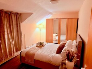 A bedroom with a bed, a bedside table with a lamp, a mirror, a wardrobe, and a window with curtains. - Charming 4-bedroom Holiday Home in Chorley (Chorley)