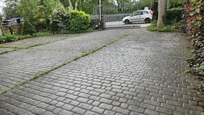 Asfaltoitu polku johtaa portilla varustetulle sisäänkäynnille, jonka lähellä on pysäköity auto.