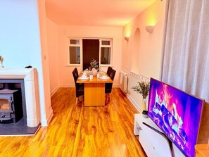A cozy living room with a fireplace, a dining table set for four, and a flat-screen TV. - Charming 4-bedroom Holiday Home in Chorley (Chorley)