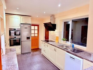 A kitchen with white cabinets, a built-in oven, a stainless steel refrigerator, a black range hood, a window with a view, and a sink with a faucet. - Charming 4-bedroom Holiday Home in Chorley (Chorley)