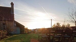 Une personne allongée sur l’herbe, avec une maison et des chaises en arrière-plan.