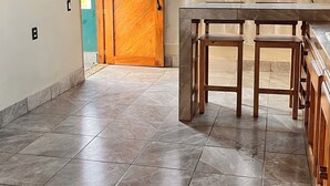 Un'ampia stanza con soffitto in legno, un'ampia finestra con tende leggere, una porta in legno con un numero e un pavimento piastrellato.