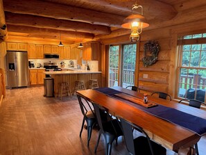 A wooden cabin interior with a kitchen, dining area, and large windows.
