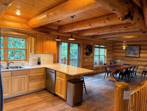 A log cabin interior with a kitchen, dining area, and large windows.