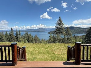 A deck with wooden railings overlooking a lake with mountains in the background.