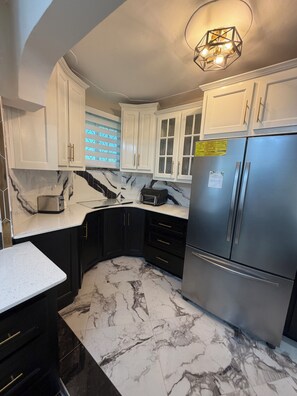 A modern kitchen with white cabinets, a stainless steel refrigerator, and a marble floor.
