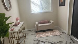 Ein Zimmer mit Marmorboden, einer Bank mit Kissen, einem kleinen Tisch mit Dekoration, einem Spiegel und einem Fenster mit Jalousien.