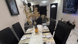 Ein Esszimmer mit einem langen Tisch, schwarzen Stühlen, einer weißen, flauschigen Tischdecke und einer Vase mit Dekorationen.