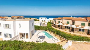 A coastal residential area with modern white buildings, a swimming pool, and a view of the sea.