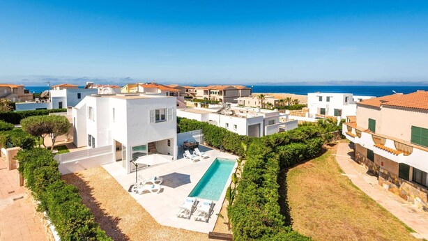 Una villa moderna con piscina, rodeada de vegetación y vistas al mar.