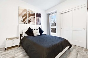 Un dormitorio con cama, mesita de noche, puerta blanca y decoración abstracta en la pared.