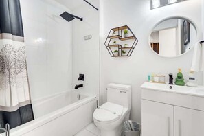 A modern bathroom with a bathtub, toilet, and vanity with a mirror. - Sunset Haven Niagara Falls | Pets | FamilyFriendly (Niagara Falls)