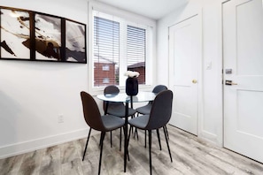 Un comedor con una mesa redonda de cristal, cuatro sillas y una ventana con persianas.
