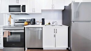 Una cucina moderna con mobili bianchi, elettrodomestici in acciaio inossidabile e una parete di fondo rivestita con piastrelle a spina di pesce.