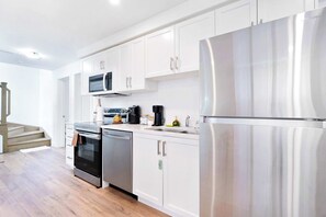 A modern kitchen with white cabinets, stainless steel appliances, and a wooden floor. - Luxury Retreat Minutes from Niagara Falls & Casino (Niagara Falls)