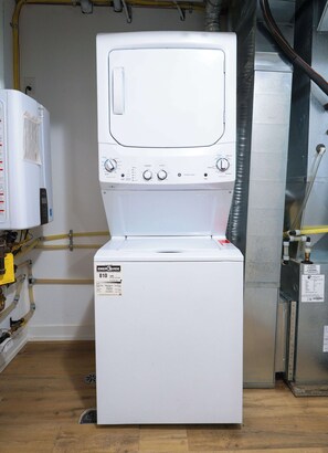 A white washer and dryer unit with control panels, a label, and visible plumbing. - Luxury Retreat Minutes from Niagara Falls & Casino (Niagara Falls)