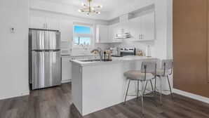 A modern kitchen with a central island, stainless steel appliances, and bar stools. - Stylish Penthouse with Rooftop & Parking Included! (Niagara Falls)