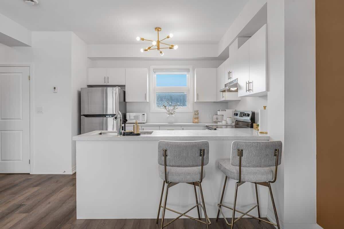 A modern kitchen with white cabinetry, a central island, two bar stools, a stainless steel refrigerator, and a pendant light.