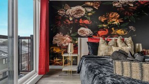 A room with a large window, a black floral wallpaper, a red curtain, a black sofa, and a small side table with a lamp. - Stylish Penthouse with Rooftop & Parking Included! (Niagara Falls)