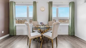A dining area with a round glass table, four chairs, a clock on the wall, and a view through large windows. - Stylish Penthouse with Rooftop & Parking Included! (Niagara Falls)
