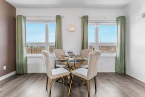 A dining area with a round glass table, four chairs, a clock on the wall, and a view through large windows. - Stylish Penthouse | Rooftop & Parking Included (Niagara Falls)