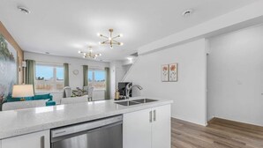A modern kitchen with white cabinetry, a stainless steel dishwasher, and a large island with a sink. - Stylish Penthouse with Rooftop & Parking Included! (Niagara Falls)