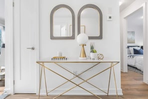 A white console table with gold accents, two mirrors, a white lamp, and a potted plant. - New 2BR Suite Sleeps 5, 7 Min to Falls w/Parking (Niagara Falls)