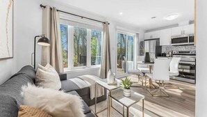 A modern living room with a sofa, a coffee table, and a view of the kitchen. - New 2BR Suite Sleeps 5, 7 Min to Falls w/Parking (Niagara Falls)