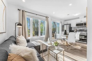 A modern living room with a sofa, a coffee table, and a view of the kitchen. - New 2BR Suite Sleeps 5, 7 Min to Falls w/Parking (Niagara Falls)