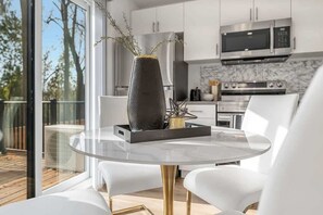 A modern kitchen with stainless steel appliances, a dining area with a glass table and white chairs, and a view of the outdoors through large windows. - New 2BR Suite Sleeps 5, 7 Min to Falls w/Parking (Niagara Falls)