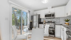 A modern kitchen with white cabinets, stainless steel appliances, and a glass dining table. - New 2BR Suite Sleeps 5, 7 Min to Falls w/Parking (Niagara Falls)