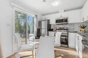 A modern kitchen with white cabinets, stainless steel appliances, and a glass dining table. - New 2BR Suite Sleeps 5, 7 Min to Falls w/Parking (Niagara Falls)
