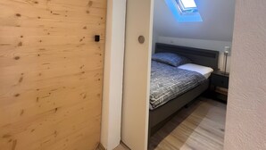 Makuuhuone, jossa on puusäleistä tehty seinä, kattovalokupu, kuviollinen vuodevaatteilla varustettu sänky, yöpöytä ja pieni sivupöytä.