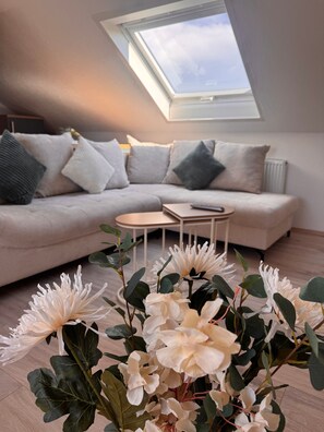 Ein modernes Wohnzimmer mit Oberlicht, einer Couch, einem Couchtisch und künstlichen Blumen.