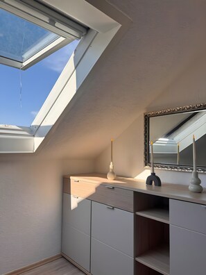 Une lucarne, un miroir et une coiffeuse avec un porte-bougie.
