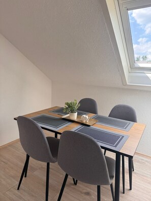 Ein Essbereich mit Tisch, Stühlen, einer Topfpflanze und Blick zum Himmel durch ein Fenster.